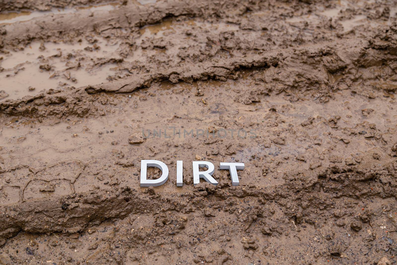 the word dirt laid with silver letters on wet dirt road surface - close-up with selective focus.