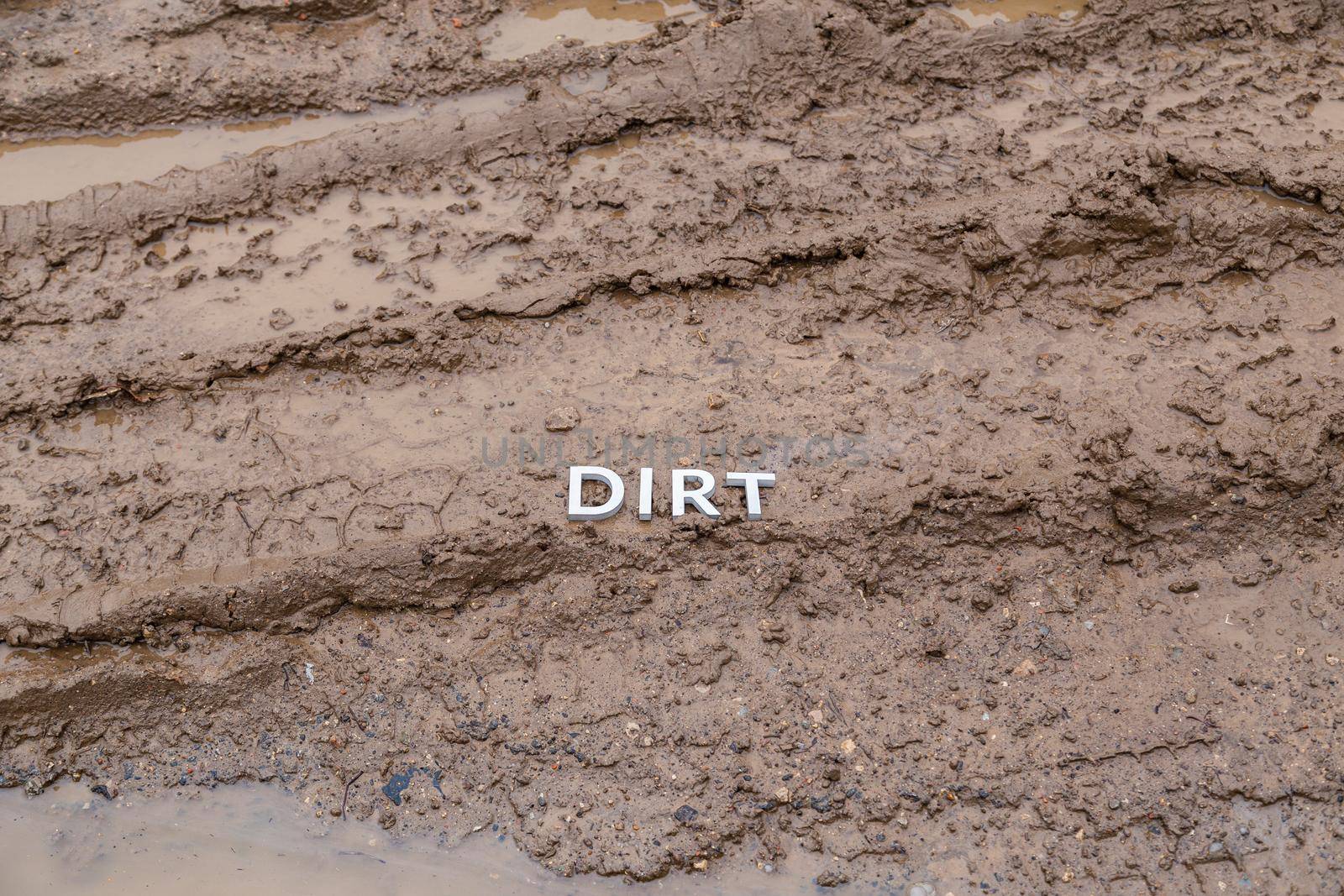 the word dirt laid with silver letters on wet dirt road surface - close-up with selective focus.