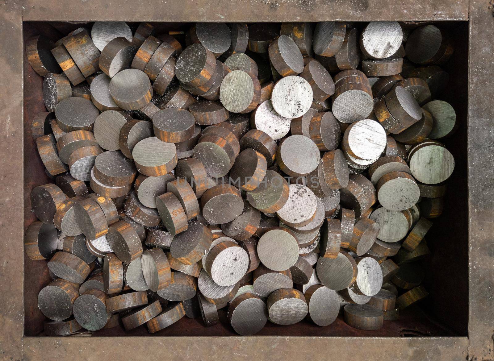 A pile of cutted with saw short cylindrical steel workpieces. Close-up abstract industrial background with rusted steel box frame.