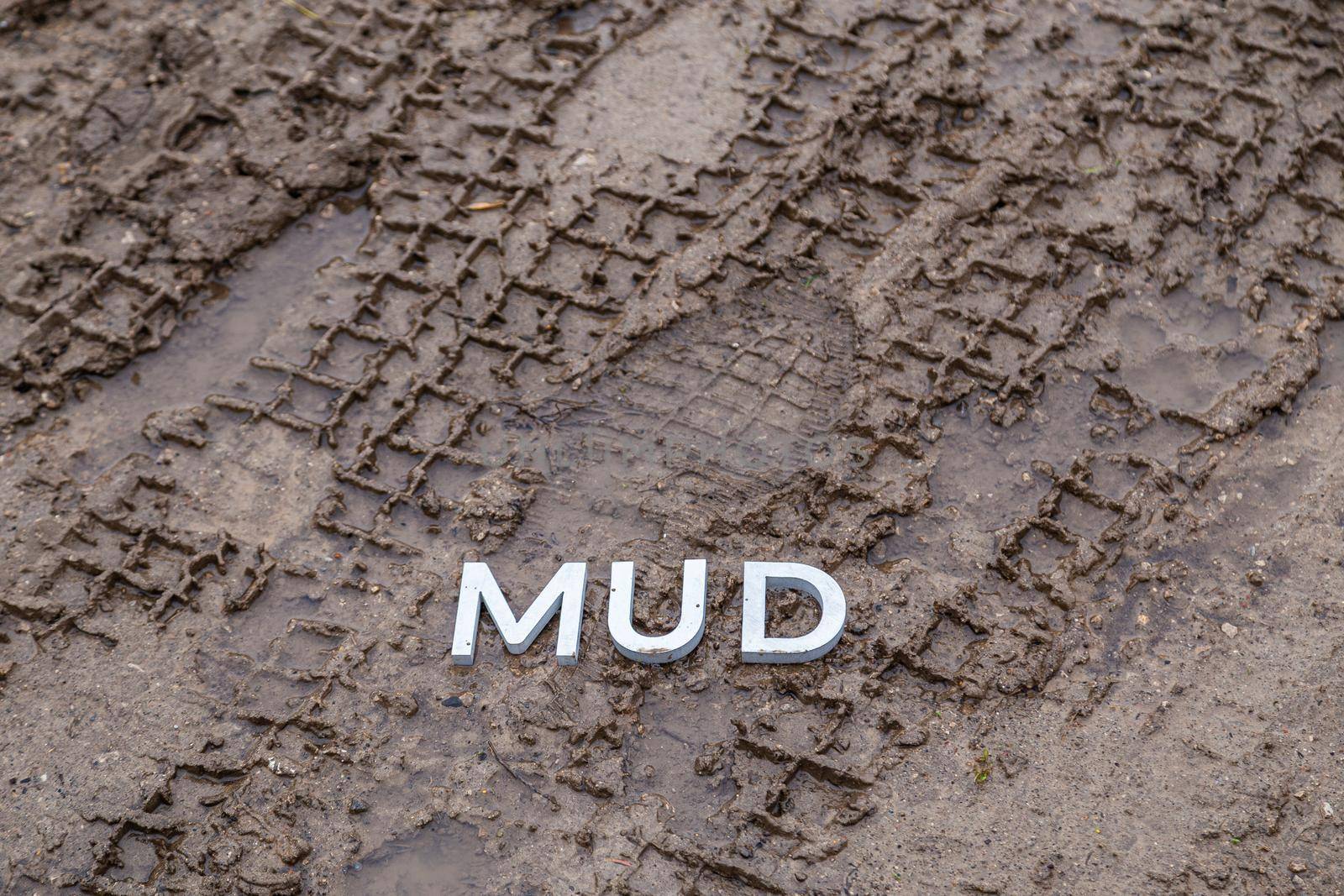 the word mud laid with silver metal letters on wet dirt surface with directly above perspective under cloudy autumn day light