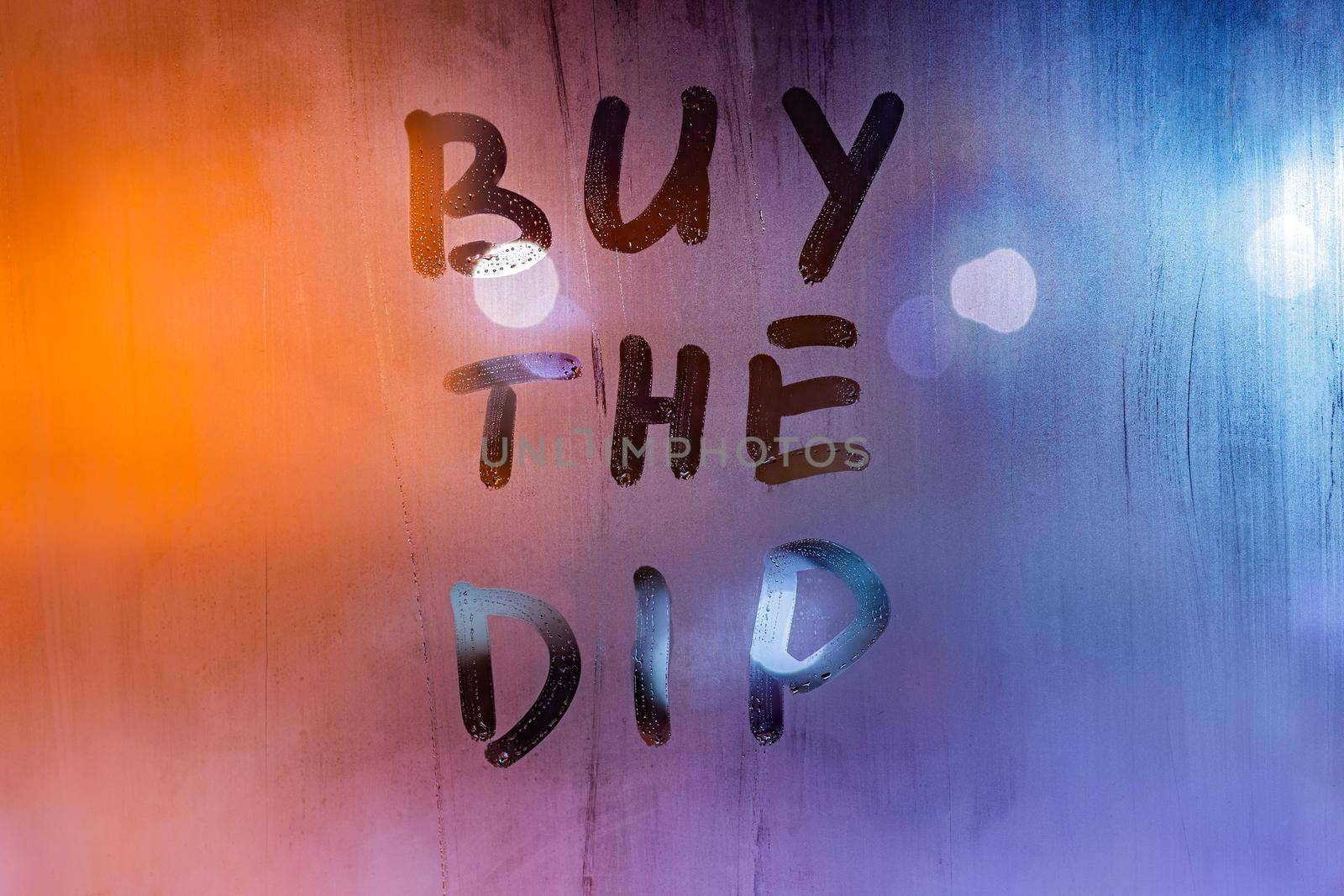phrase buy the dip handwritten on night wet window glass surface - close-up with selective focus