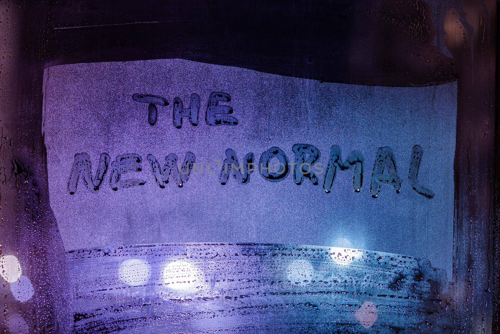words the new normal handwritten on wet night window glass, close-up with selective focus
