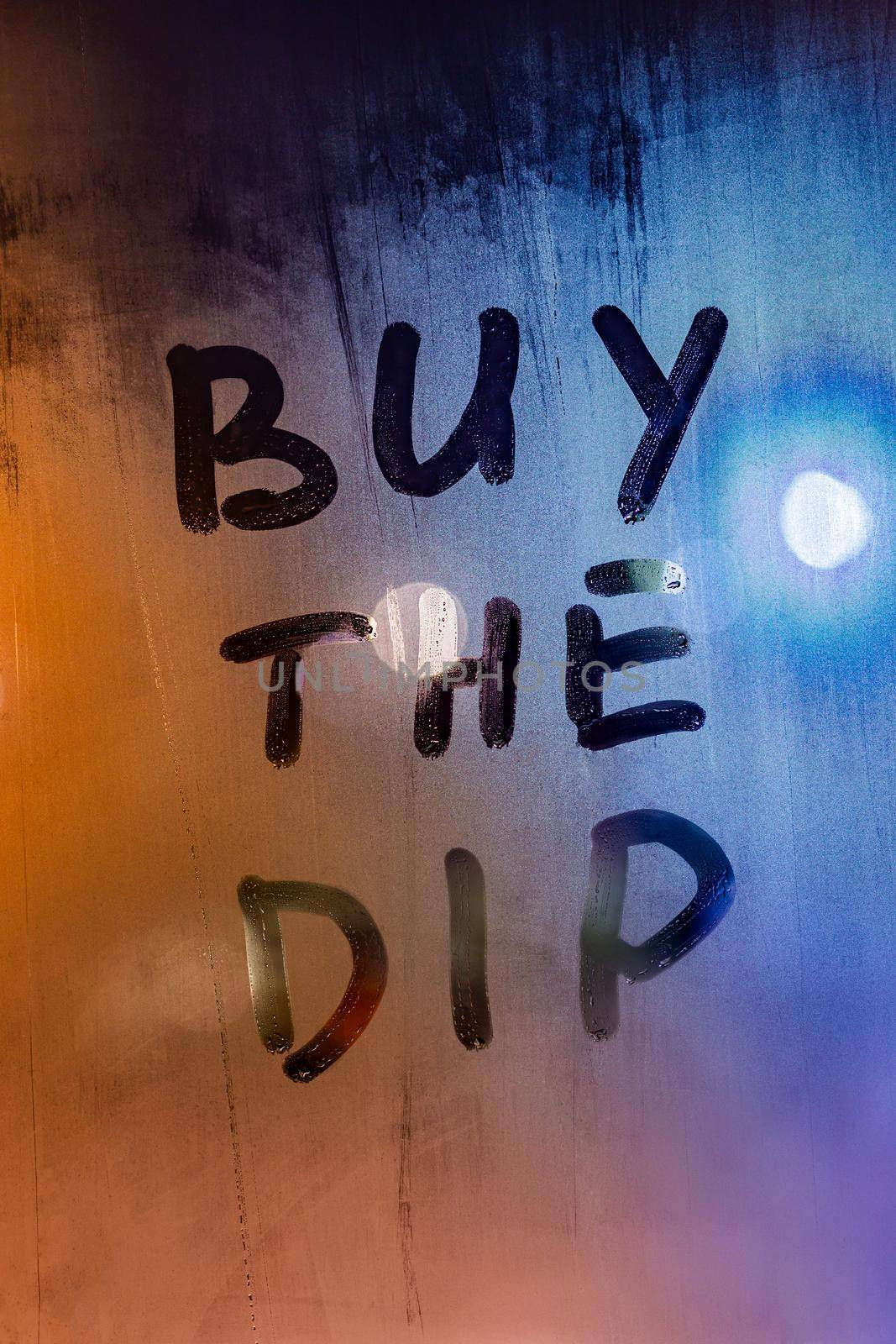 phrase buy the dip handwritten on night wet window glass surface - close-up with selective focus