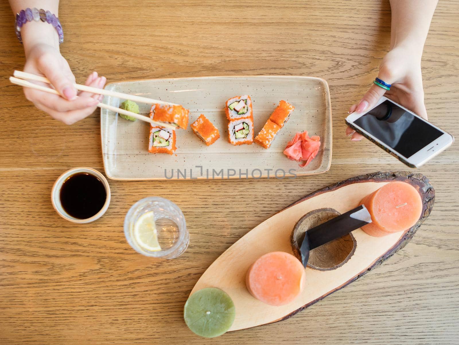 Woman eating sushi and using smartphone, top view