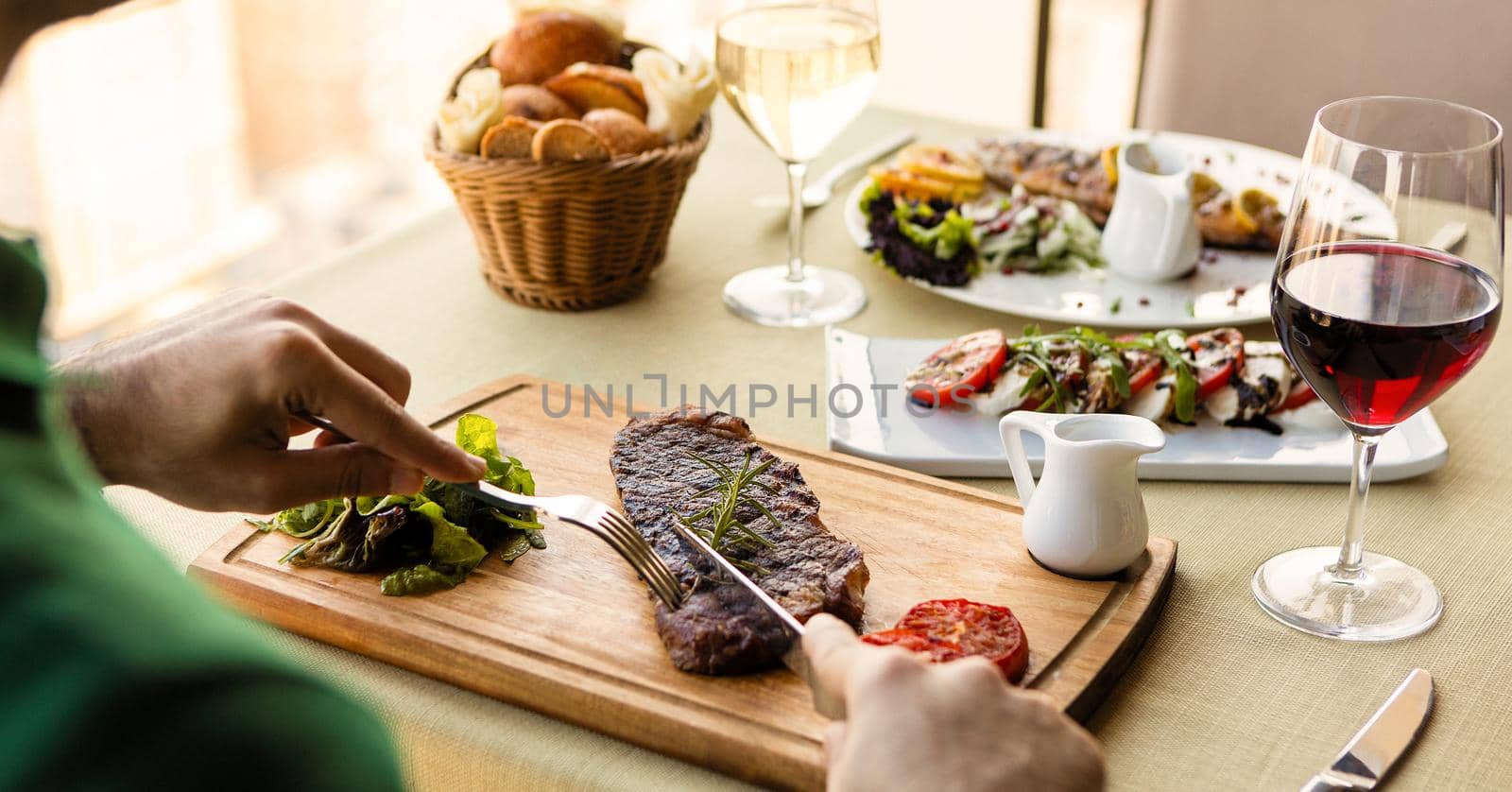 Man cutting tasty steak with sauce, salad on the table