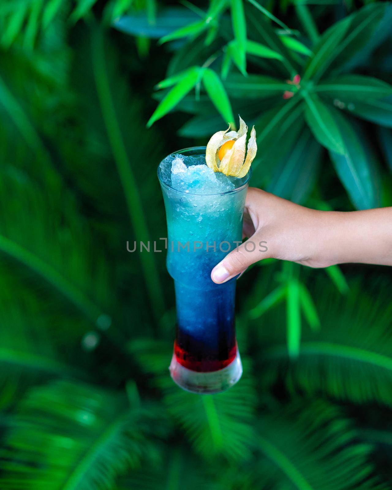 Woman holding blue colored cocktail with green background