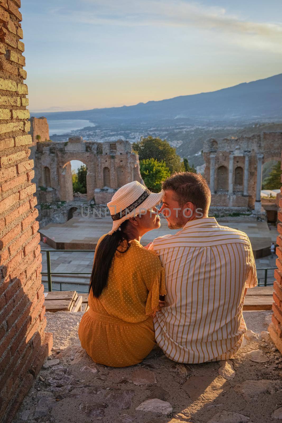 couple men and woman visit Ruins of Ancient Greek theatre in Taormina on background of Etna Volcano, Italy. Taormina located in Metropolitan City of Messina, on east coast of island of Sicily Italy