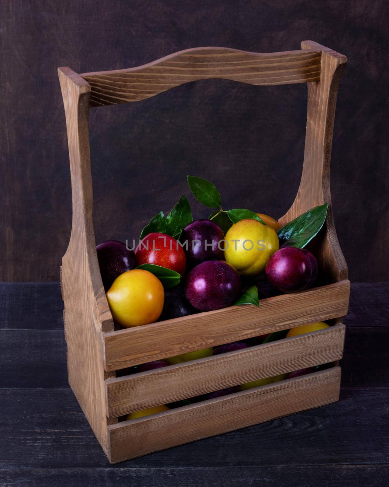 Colorful plums fruit in a wood basket on the black background isolated