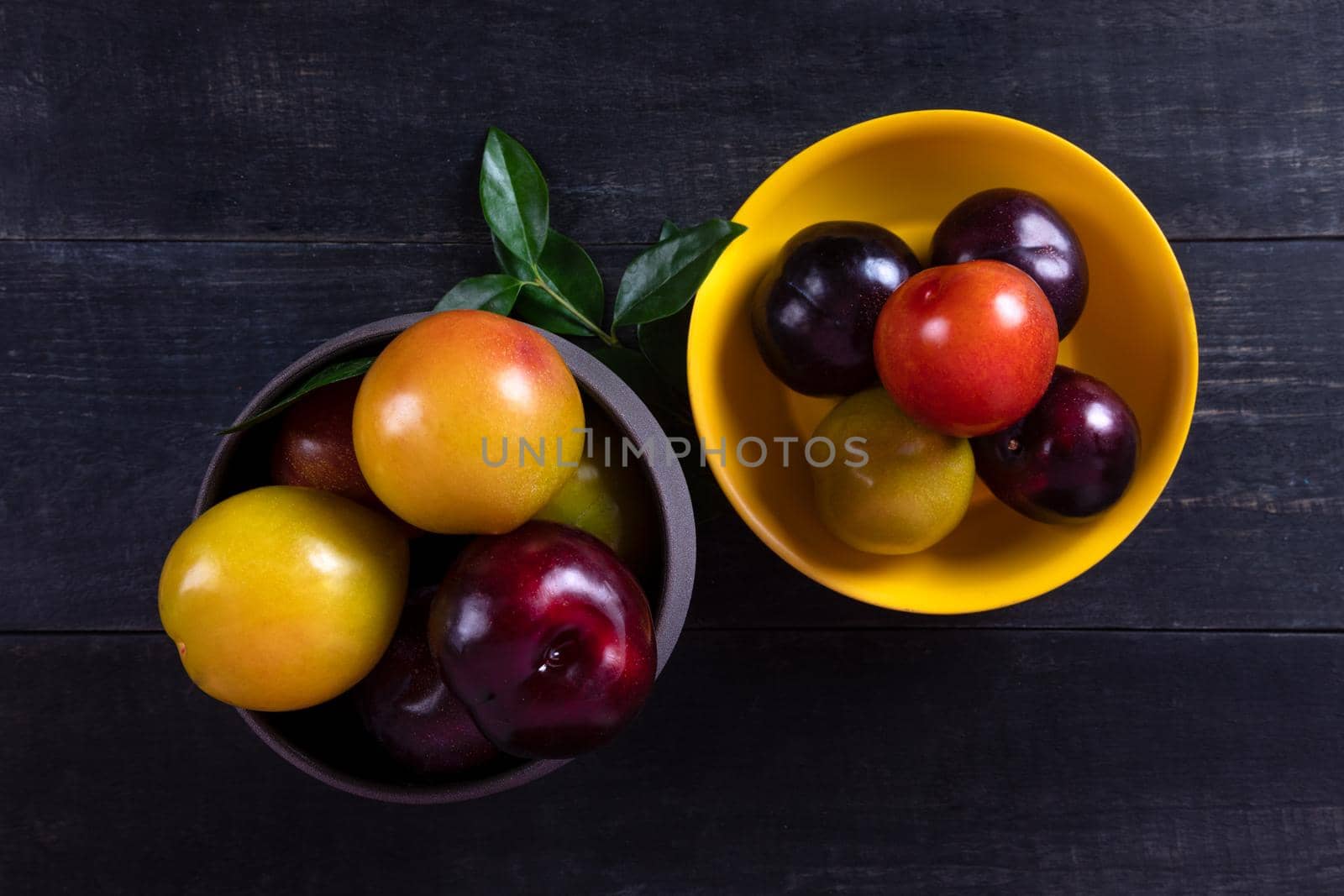Colorful plums fruit in pot and plate on the dark background top view by ferhad