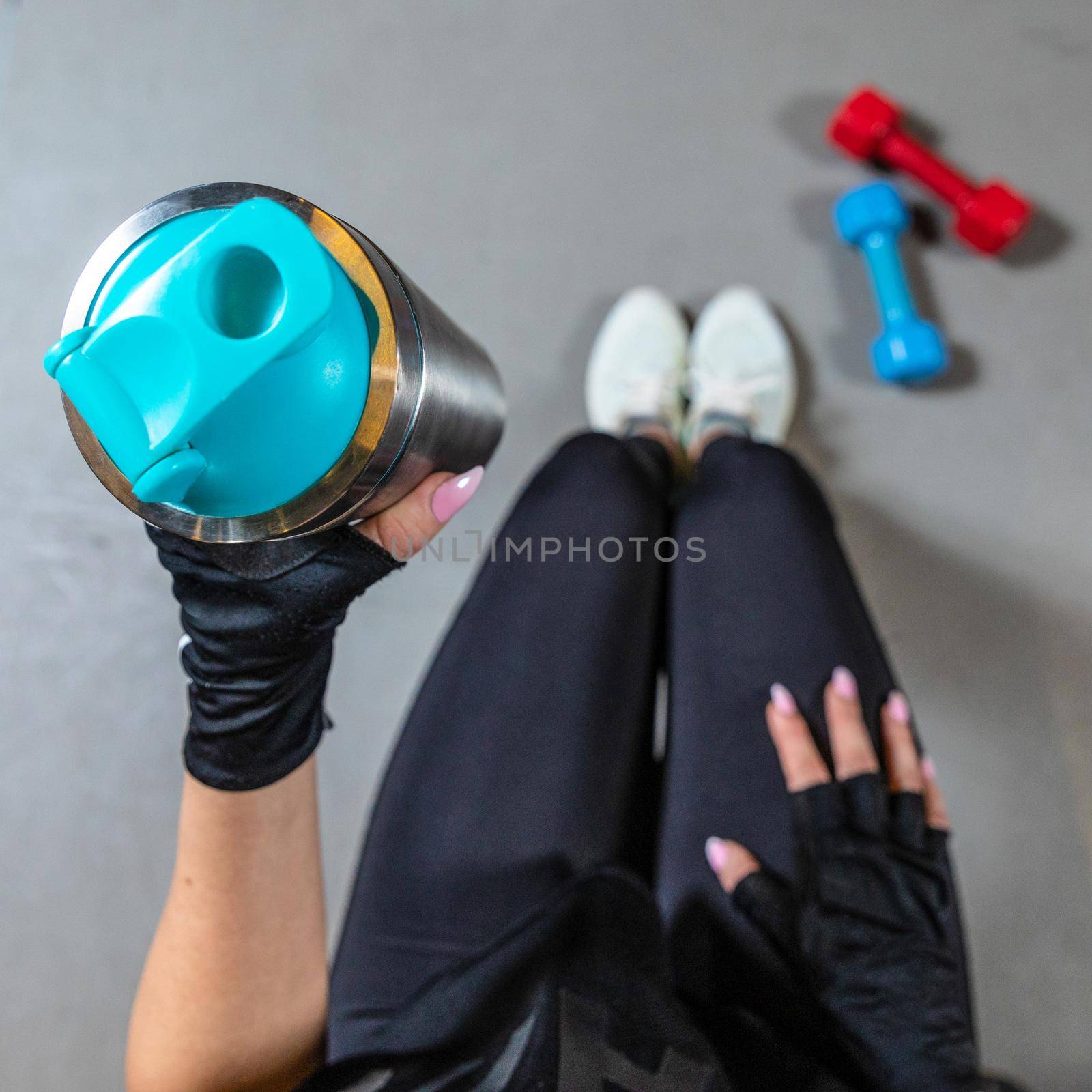 Cropped photo of fitness woman sitting in gym and holding bottle of water