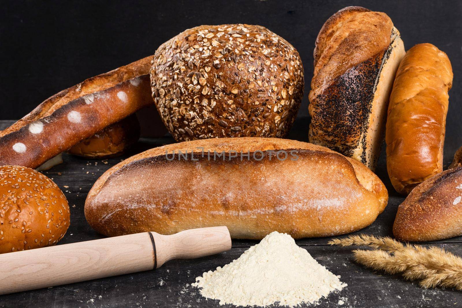 Fresh loaves of bread with flour wheat and gluten on a dark background
