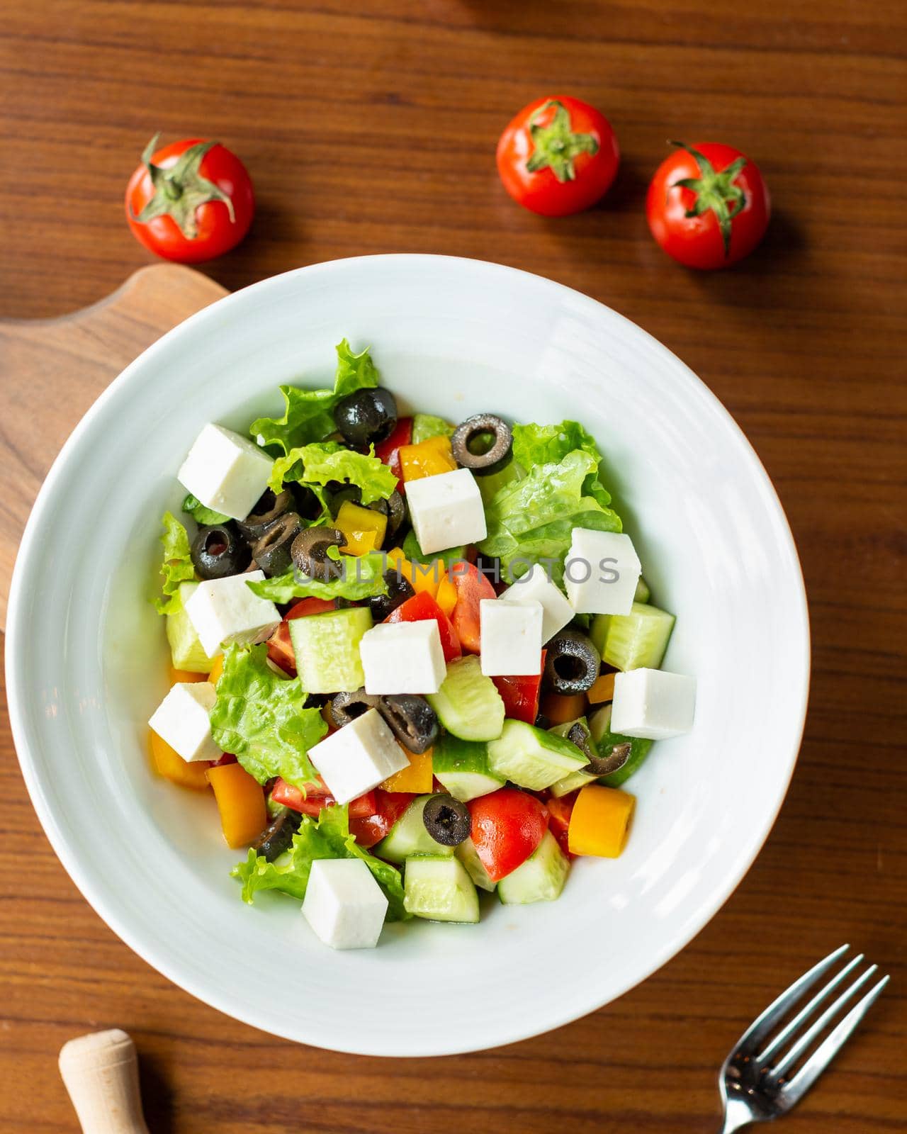 Greek salad in the white plate with tomatoes from top