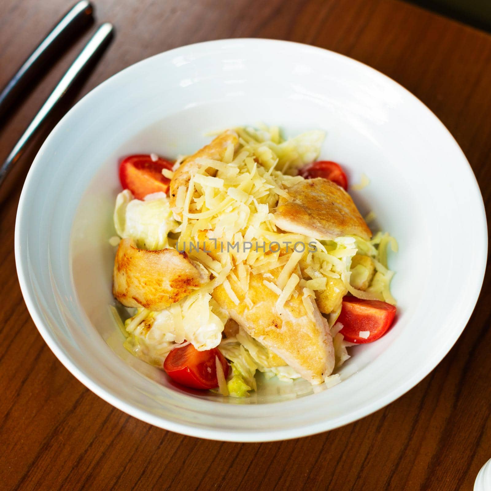 Caesar salad in the white plate with tomatoes from top