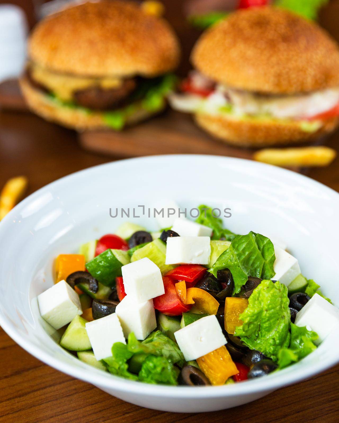 Greek salad in the white plate with burgers
