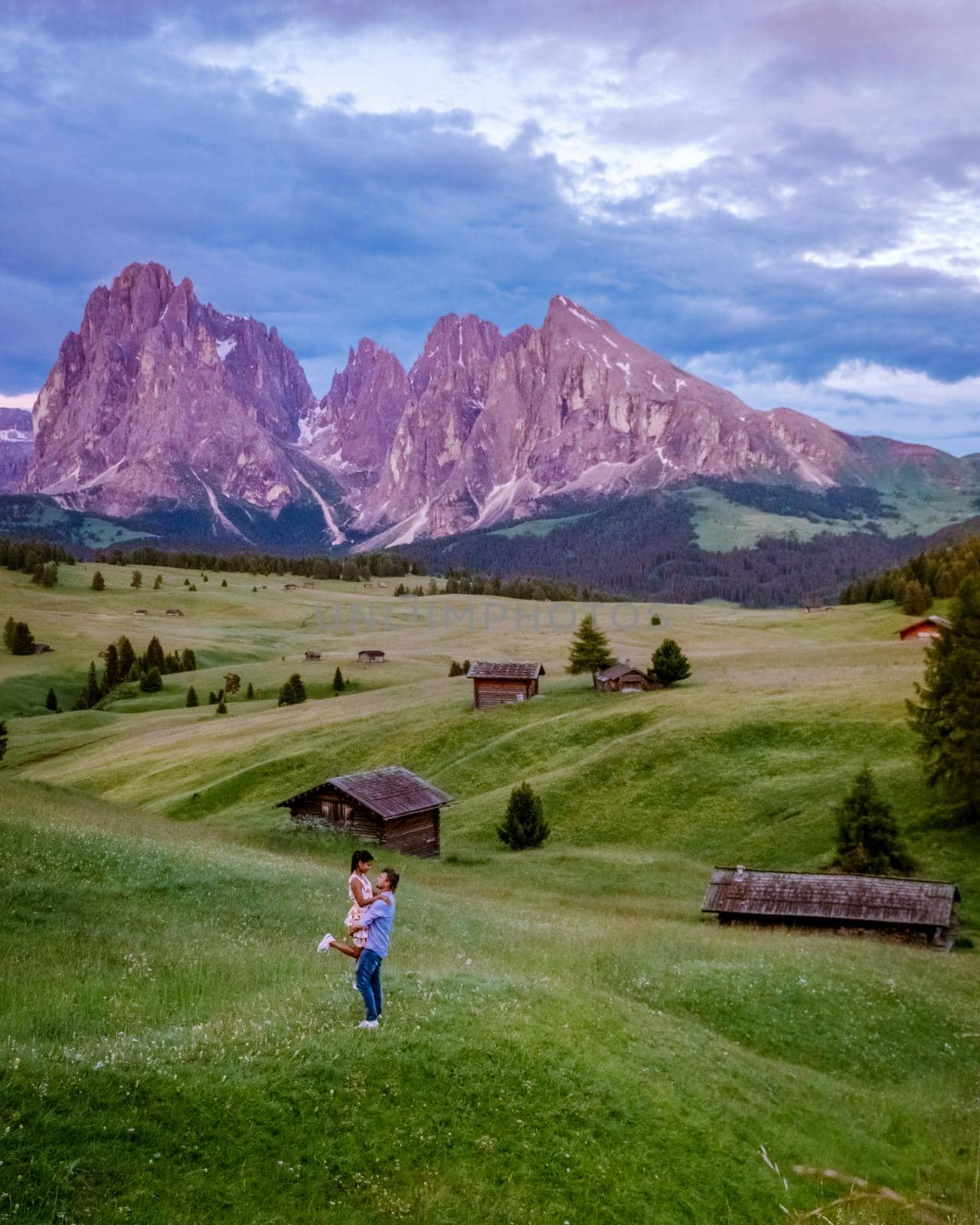 couple men and woman on vacation in the Dolomites Italy,Alpe di Siusi - Seiser Alm with Sassolungo - Langkofel mountain group in background at sunset. Yellow spring flowers and wooden chalets in Dolomites, Trentino Alto Adige, South Tyrol, Italy, Europe by fokkebok
