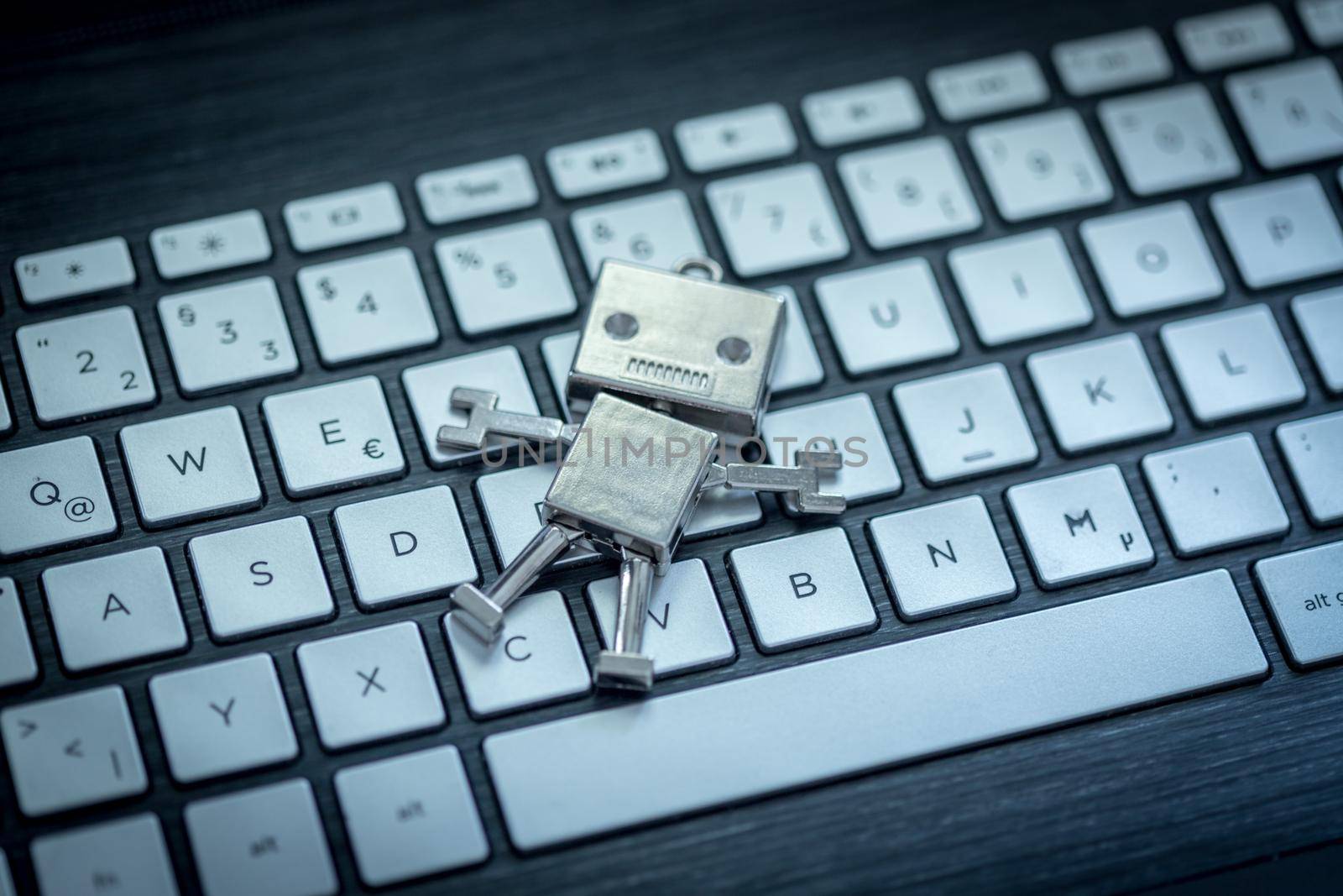 Close up of a toy robot lying on a computer keyboard. Chat bot or social bot.