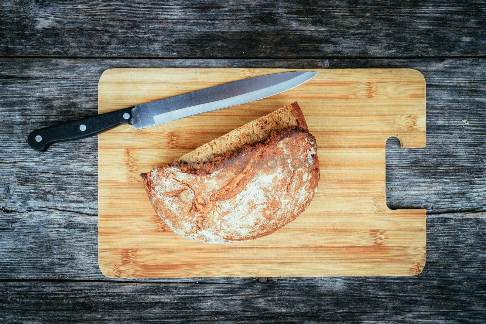 Fresh dark bread in slices. Wooden cutting board and table, knife.