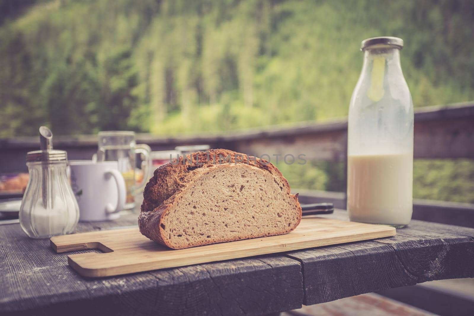 Fresh dark crisp bread for breakfast on an alpine hut. Wooden cutting board and milk in glass bottle.