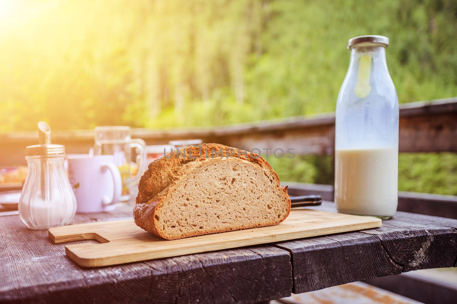 Fresh dark crisp bread for breakfast on an alpine hut. Wooden cutting board and milk in glass bottle. Sunshine.