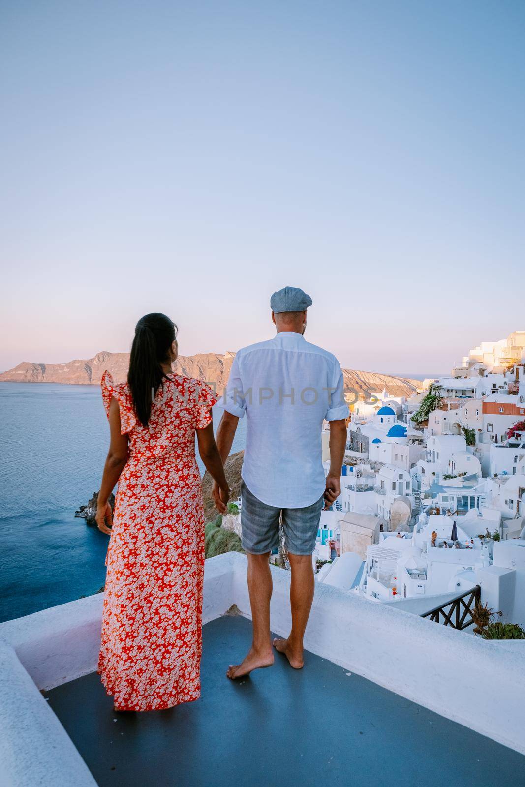 Santorini Greece, young couple on luxury vacation at the Island of Santorini watching sunrise by the blue dome church and whitewashed village of Oia Santorini Greece during sunrise during summer vacation, men and woman on holiday in Greece