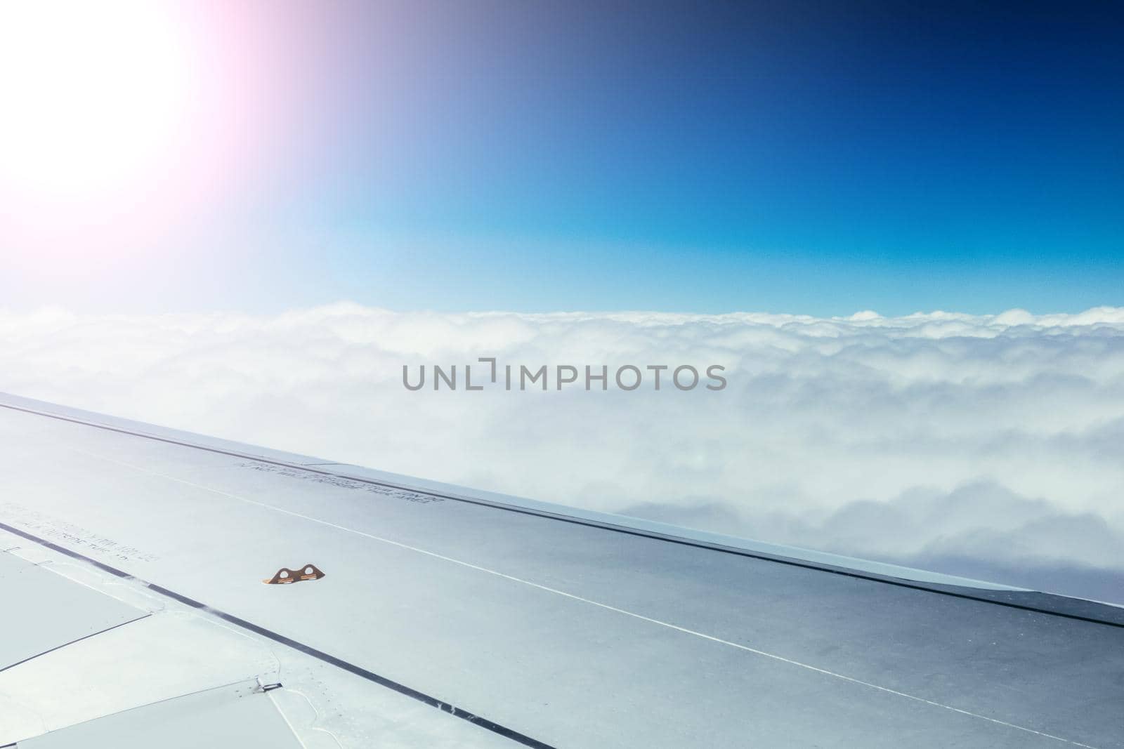 View of a grey airplane wing through the aircraft window. Sunshine, global warming.