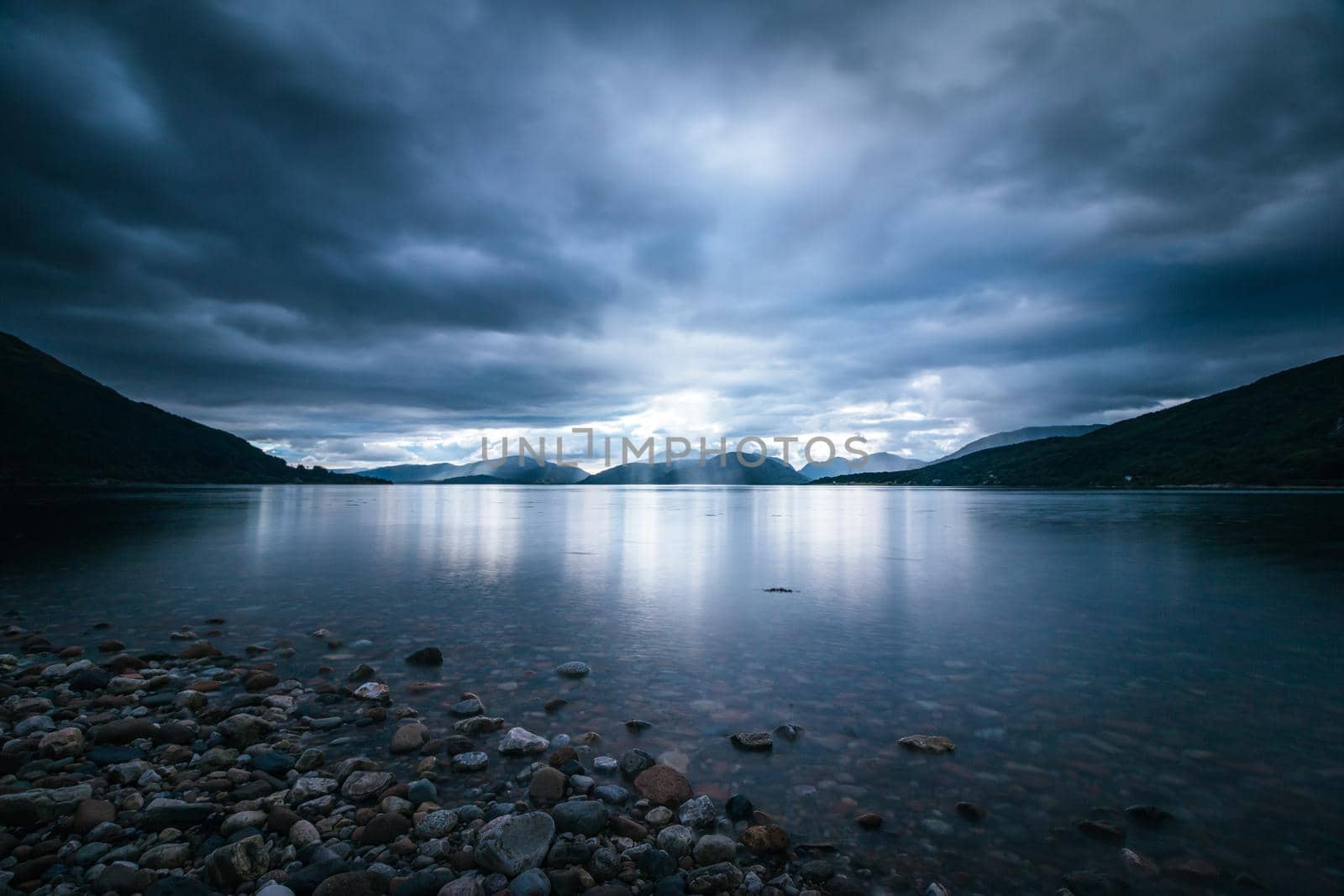 Beautiful mystic landscape lake scenery in Scotland with cloudy sky and sunbeams