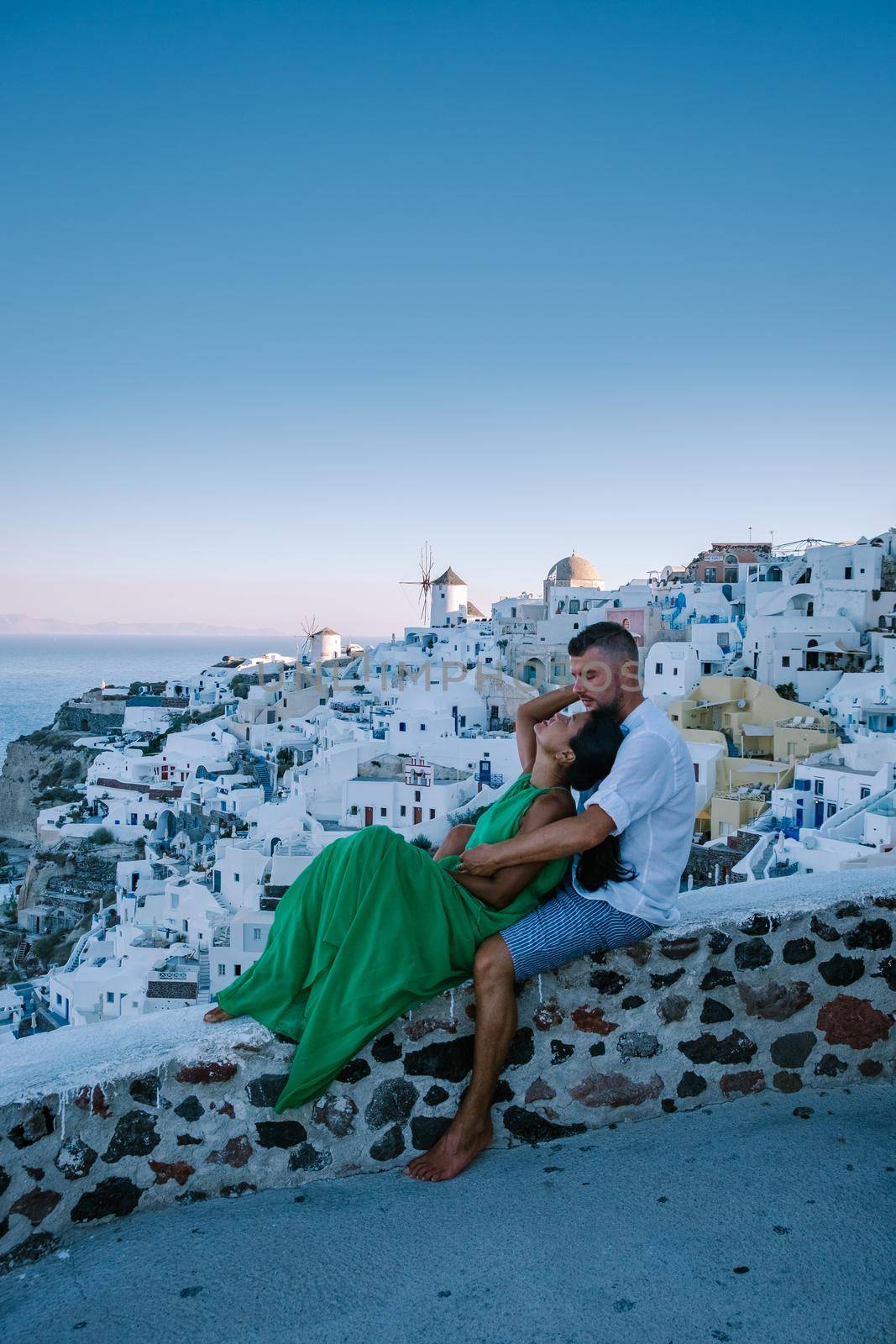 Santorini Greece, young couple on luxury vacation at the Island of Santorini watching sunrise by the blue dome church and whitewashed village of Oia Santorini Greece during sunrise, men and woman on holiday in Greece by fokkebok