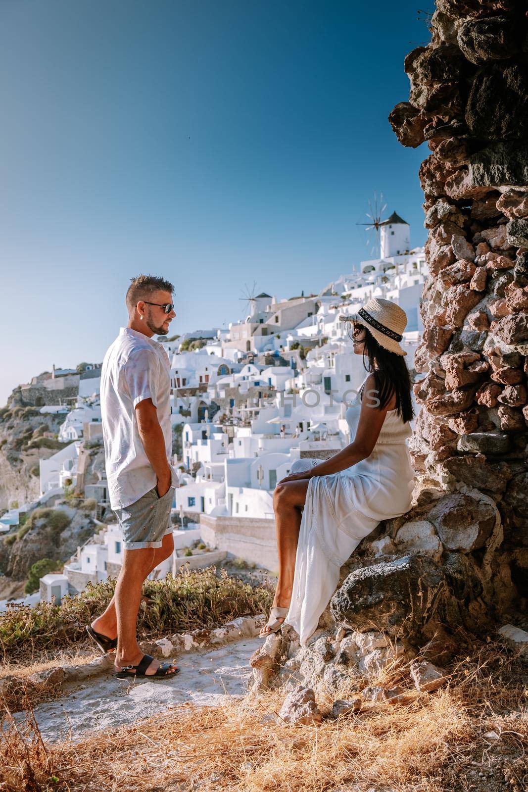 Santorini Greece, young couple on luxury vacation at the Island of Santorini watching sunrise by the blue dome church and whitewashed village of Oia Santorini Greece during sunrise during summer vacation, men and woman on holiday in Greece