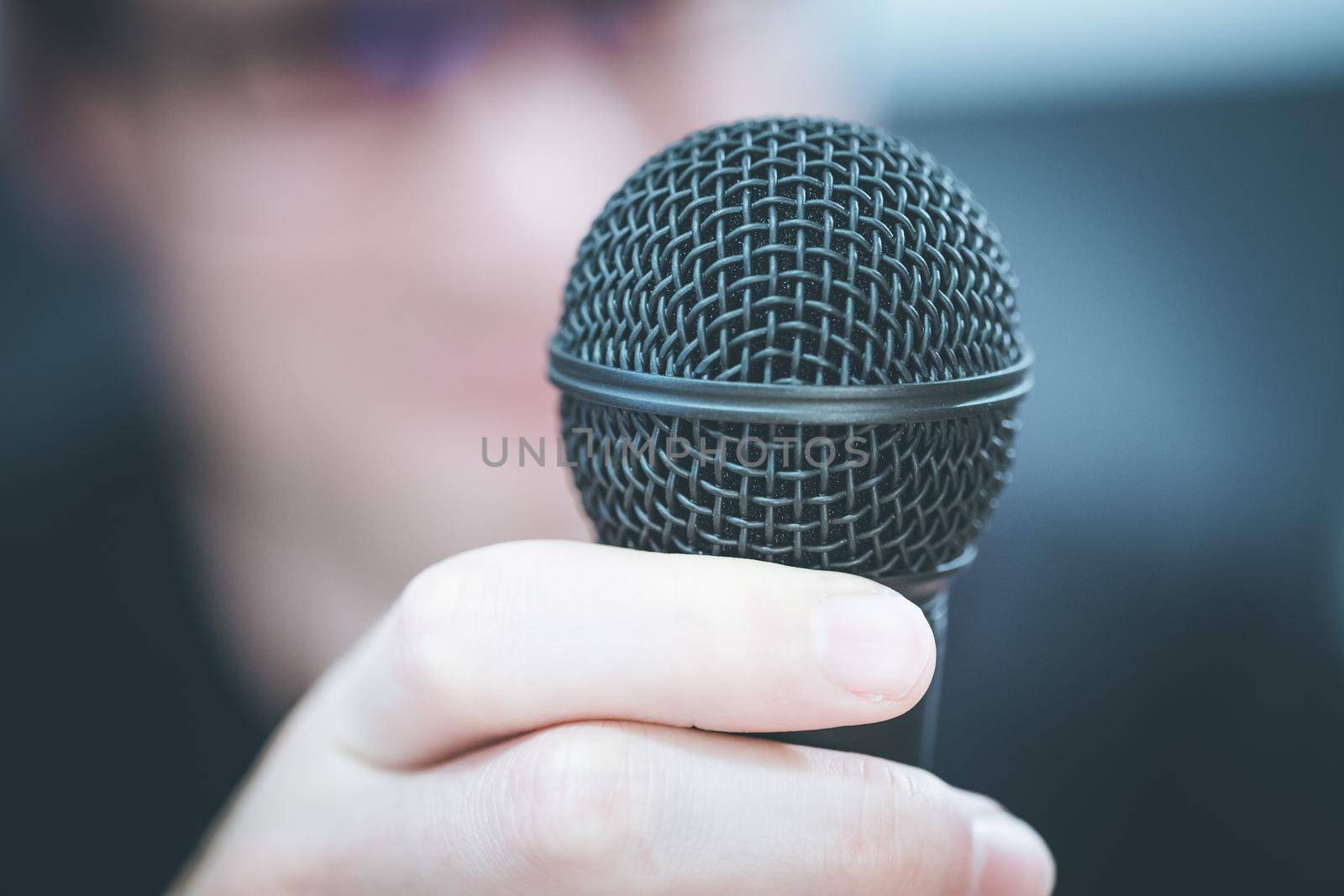 Speaking in the microphone: Young man with blurry face is taking into the microphone by Daxenbichler