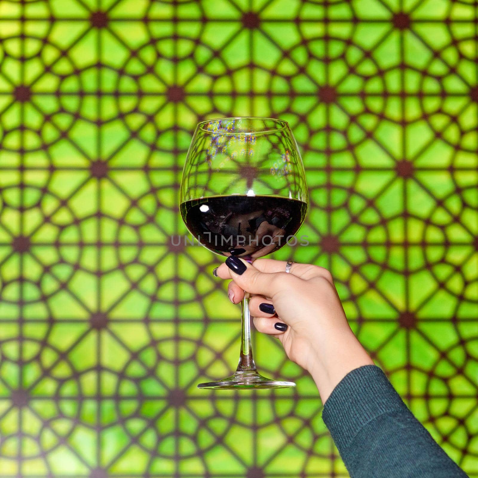 Woman holding a red wine glass with Arabic patterned background