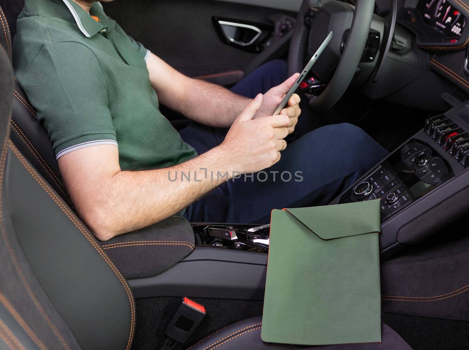 A young man with a tablet in his hand at the sports car. Multitasking