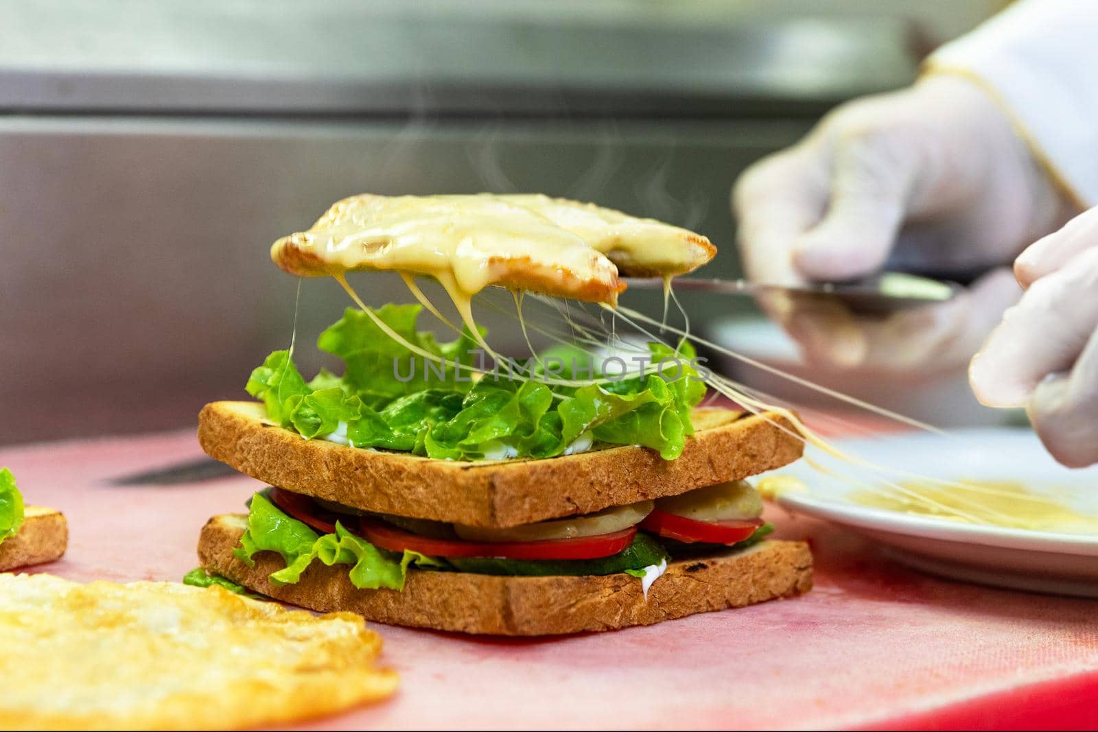 Chef in restaurant kitchen making cheesy club sandwich