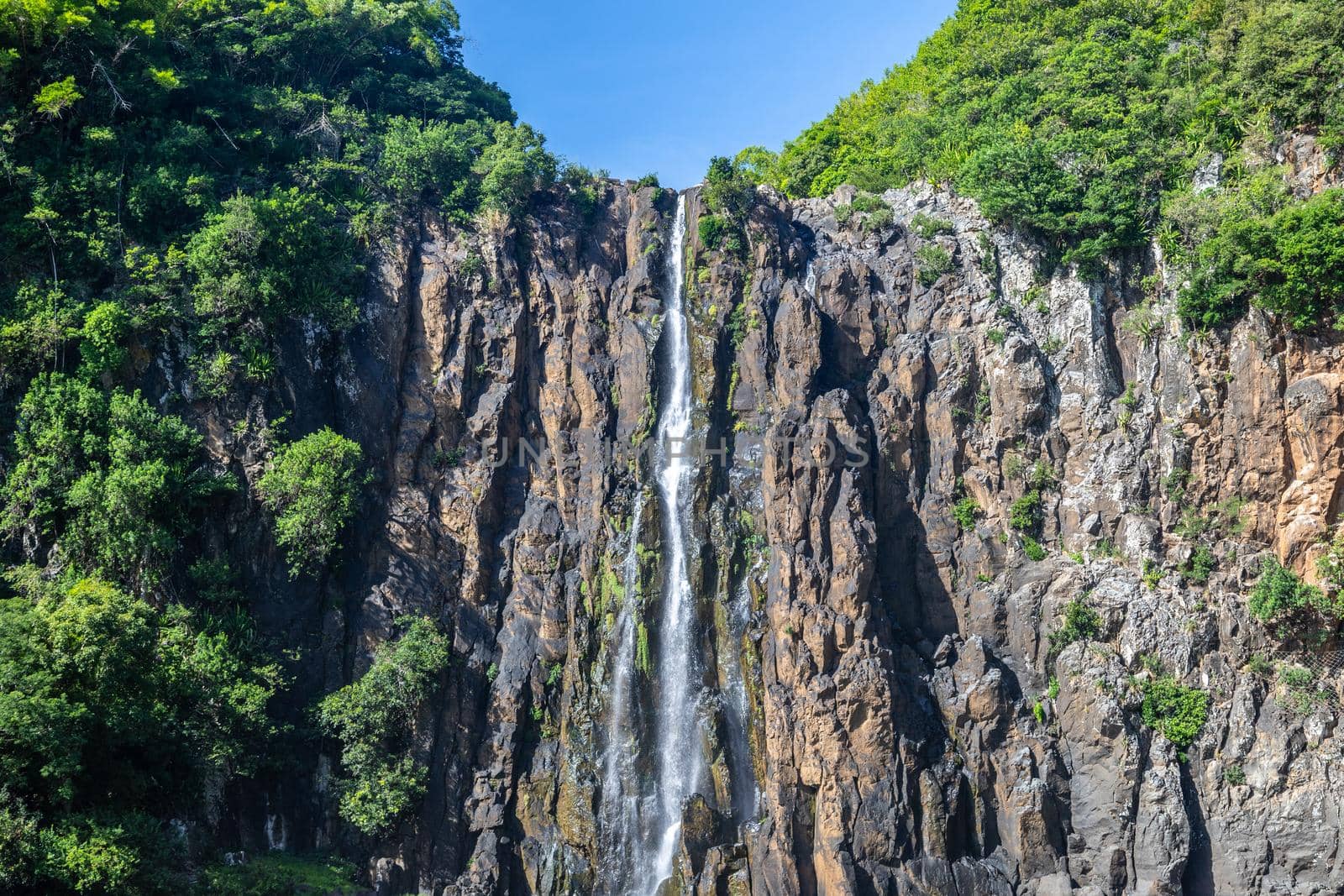 Rockface with waterfall Cascade Niagara at french island Reunion in the indian ocean on a sunny day with blue sky