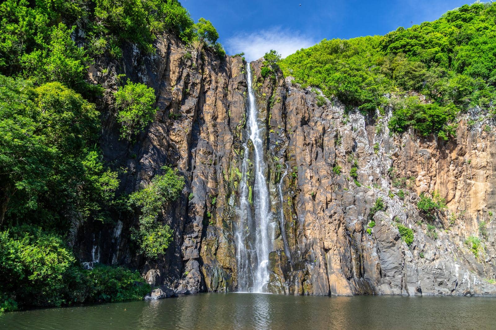 Rockface with waterfall Cascade Niagara at french island Reunion in the indian ocean on a sunny day with blue sky