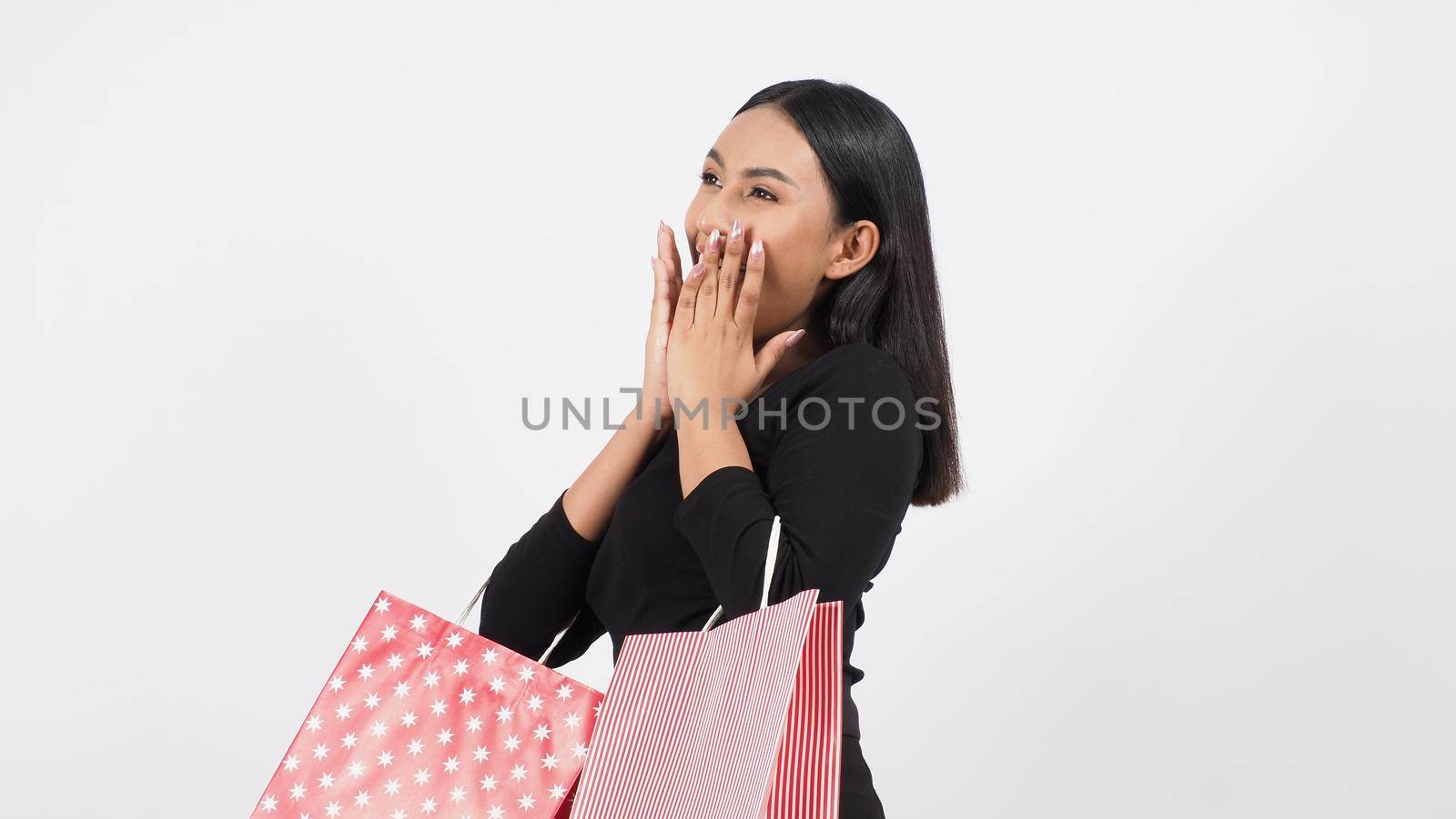 Sexy woman shopping. Portrait of excited beautiful girl wearing black holding red shopping bags isolated over white background. Cheerful happy lady enjoy carrying goods bags. half body.