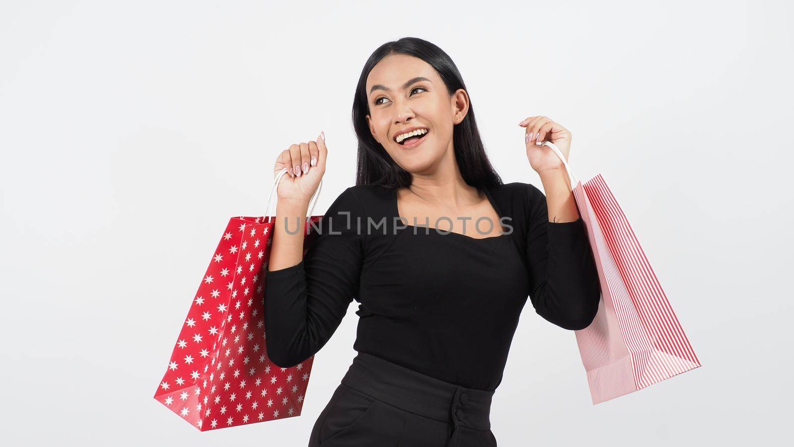 Sexy woman shopping. Portrait of excited beautiful girl wearing black holding red shopping bags isolated over white background. Cheerful happy lady enjoy carrying goods bags. half body.