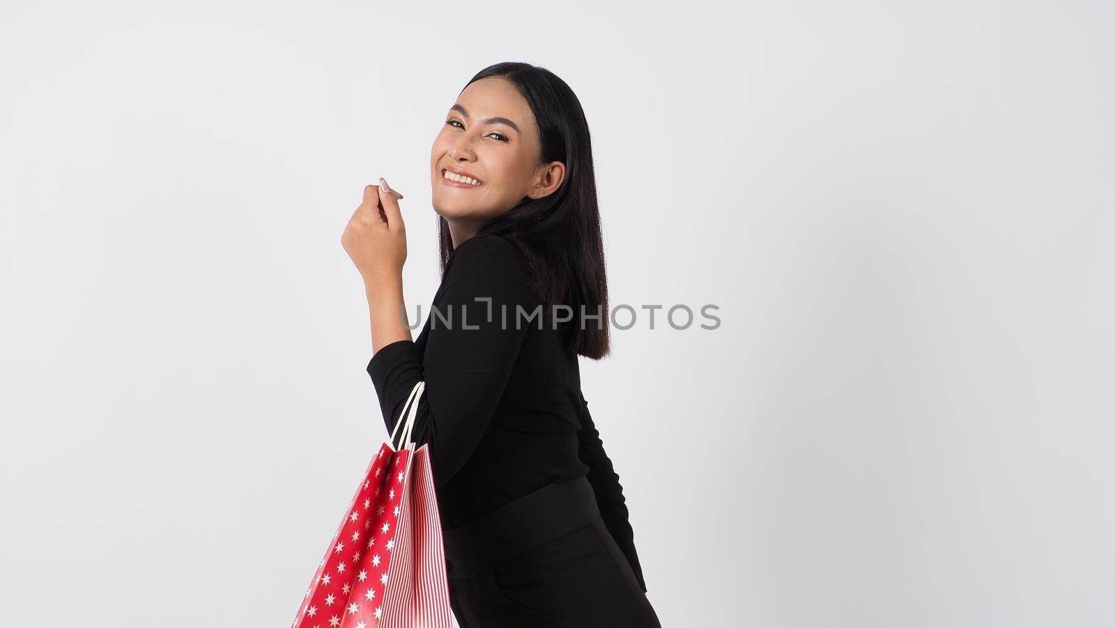 Sexy woman shopping. Portrait of excited beautiful girl wearing black holding red shopping bags isolated over white background. Cheerful happy lady enjoy carrying goods bags. half body.