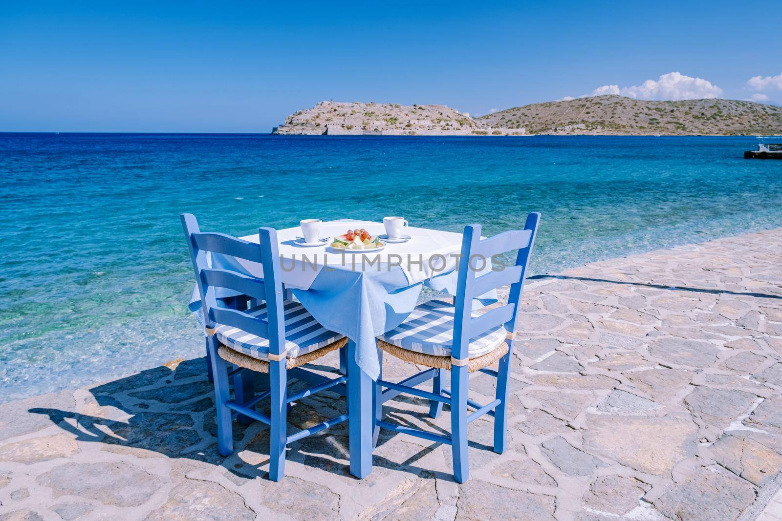 Plaka Lassithi with is traditional blue table and chairs and the beach in Crete Greece by fokkebok