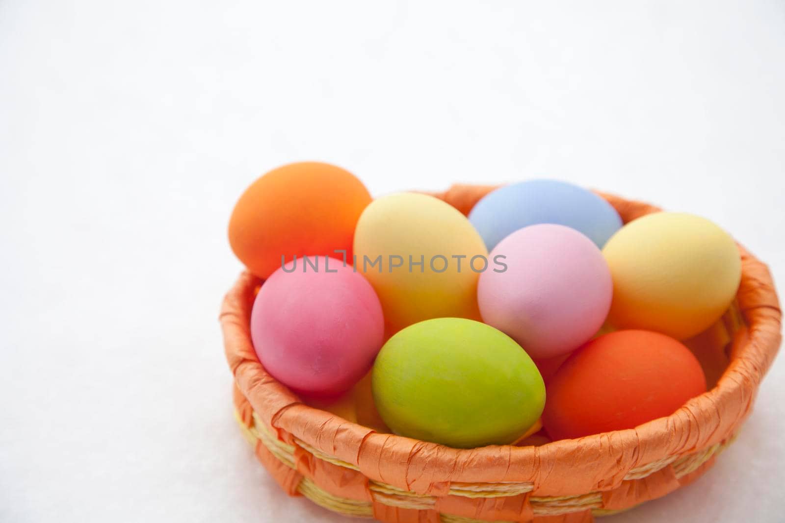 Basket with many multi colored Easter eggs lying in the snow by Kasparart
