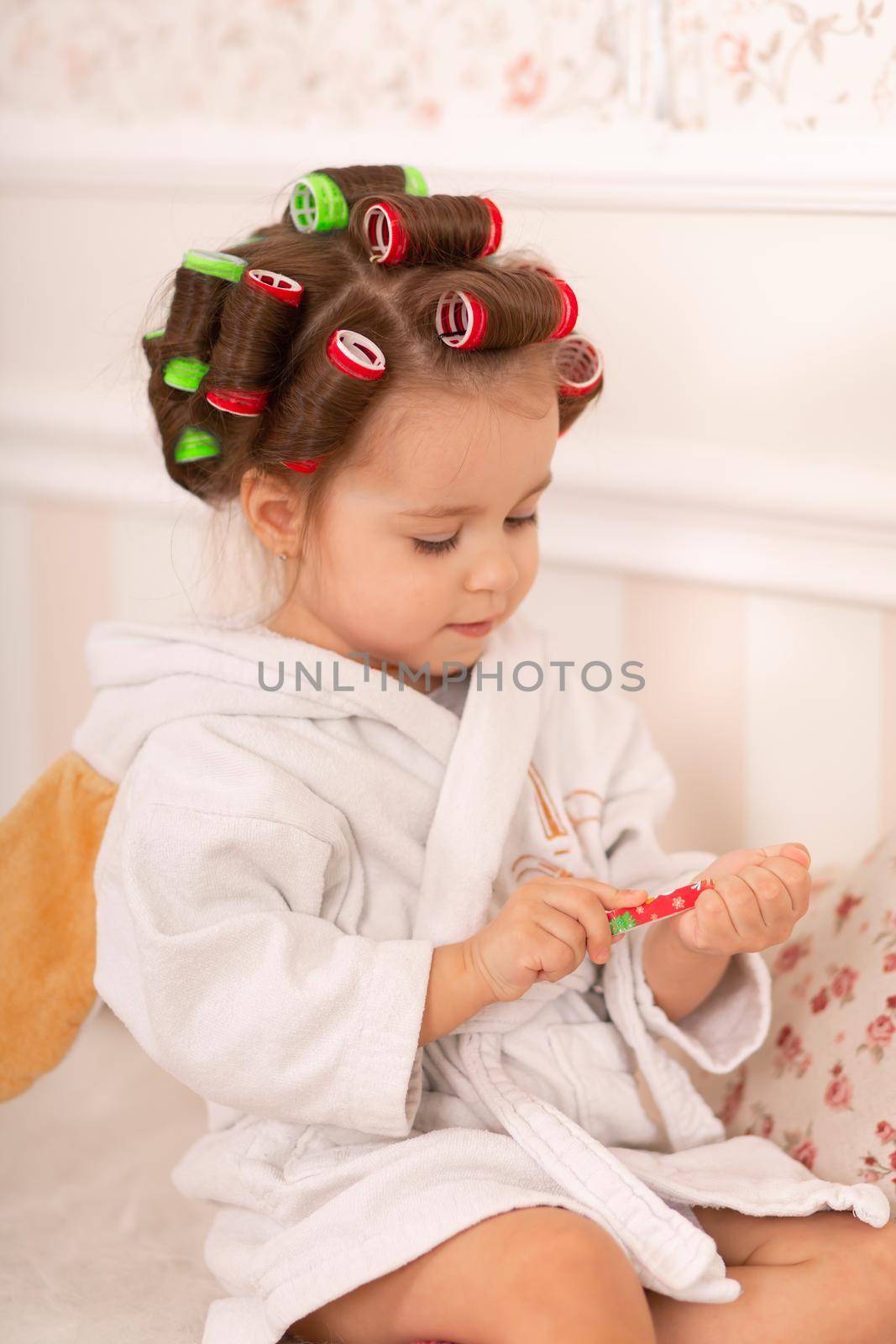 Adorable little girl with curlers paints her fingernails. Copies mom's behavior. Young fashionista. Beauty day.