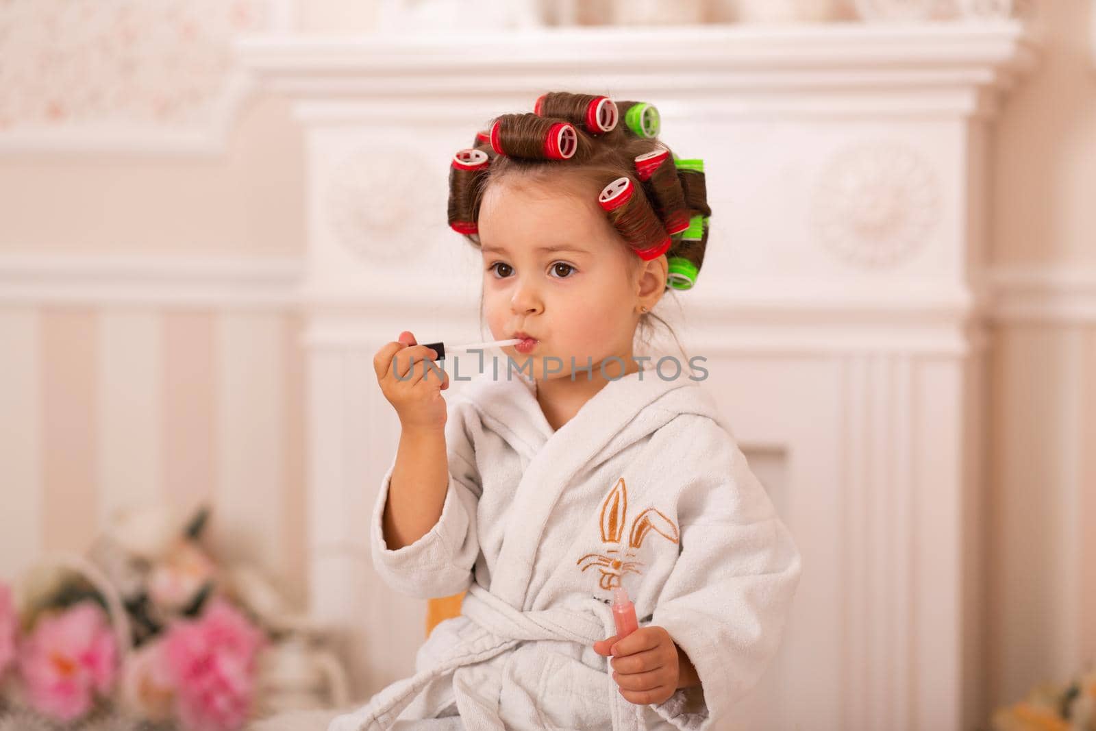 Adorable little girl with her mother in hair curlers apply makeup. Mom teaches daughter to use cosmetics. Beauty day. Girls are such girls.