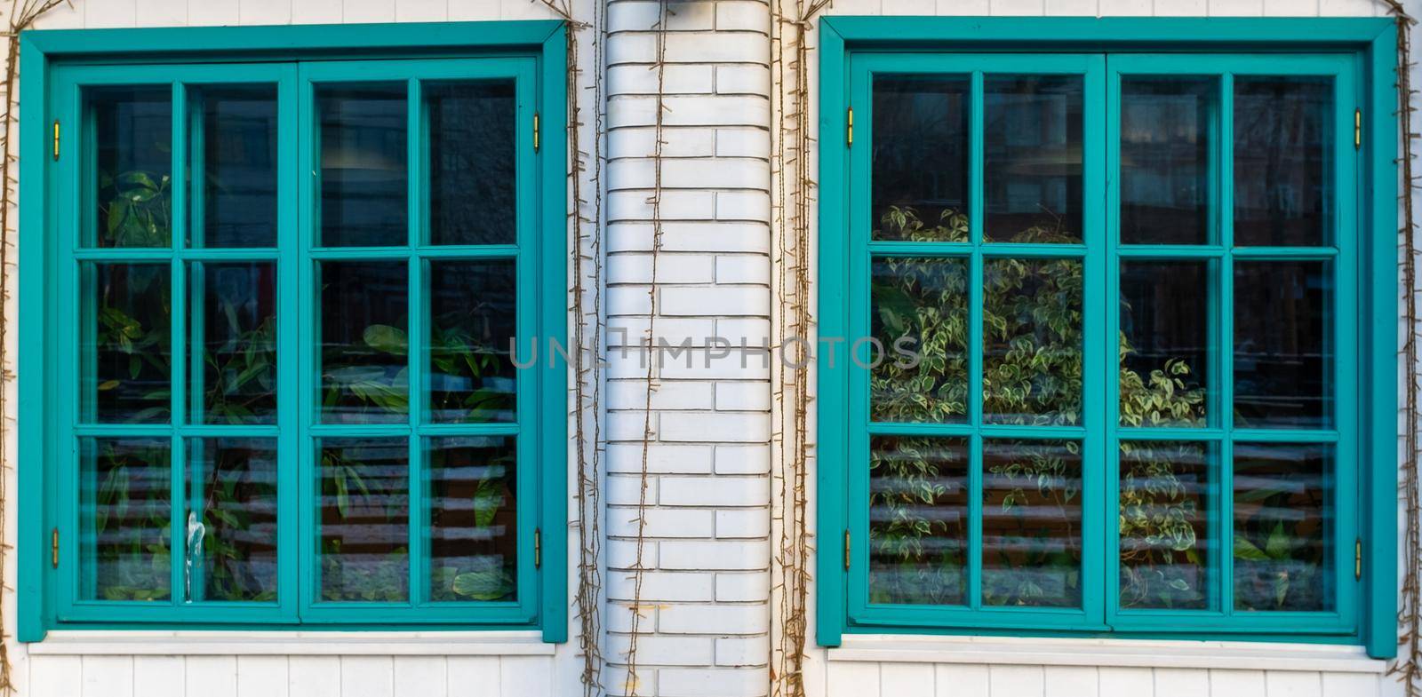 Two large turquoise windows on the veranda of a brick house.