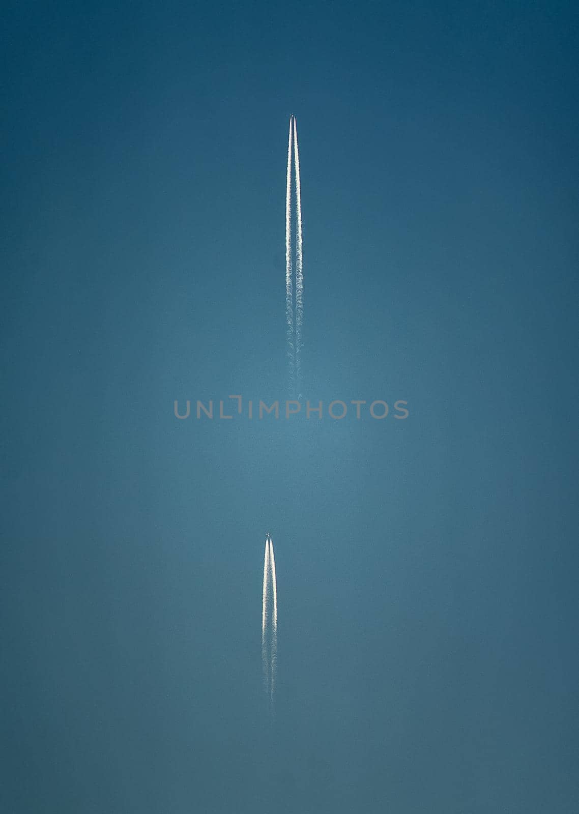 Two planes with long white condensation trails behind them high in the blue sky.