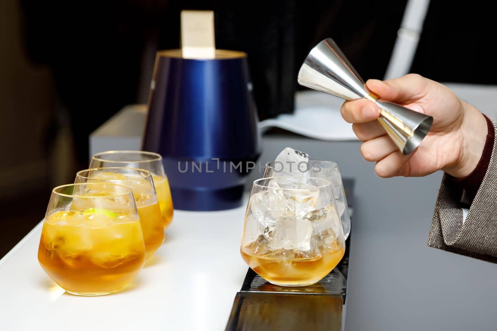 The bartender makes a cocktail. The barmen pour alcohol from a steel measuring glass