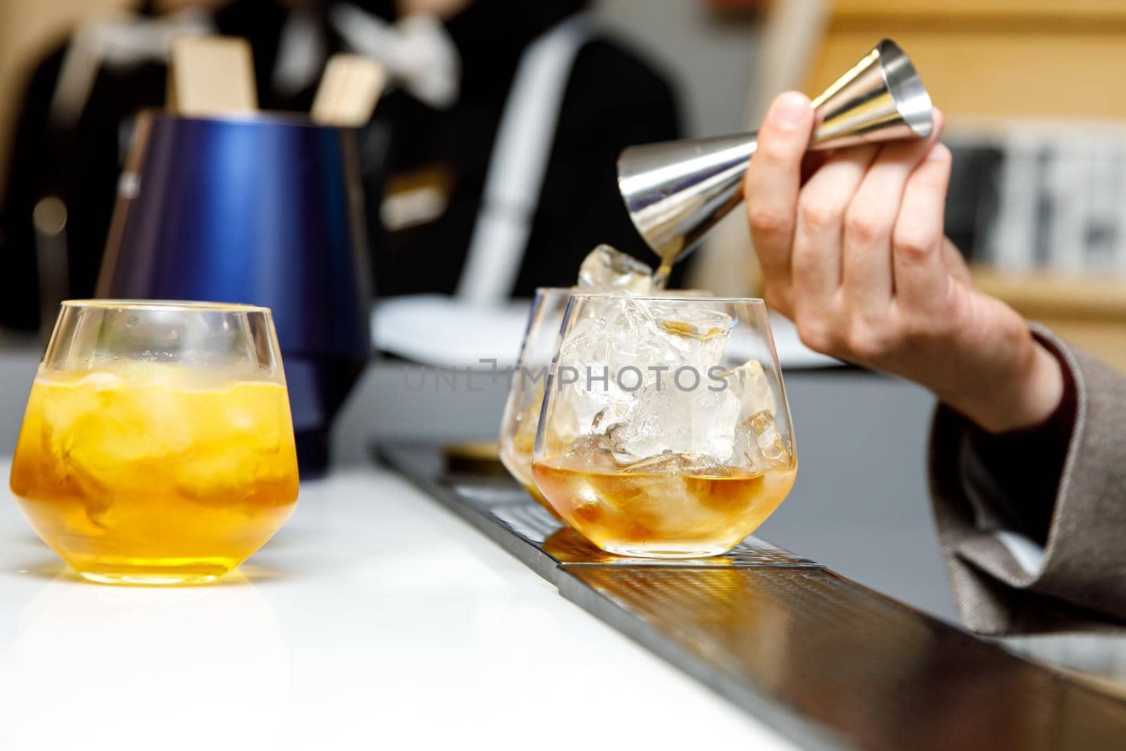 The bartender makes a cocktail. The barmen pour alcohol from a steel measuring glass. by 9parusnikov