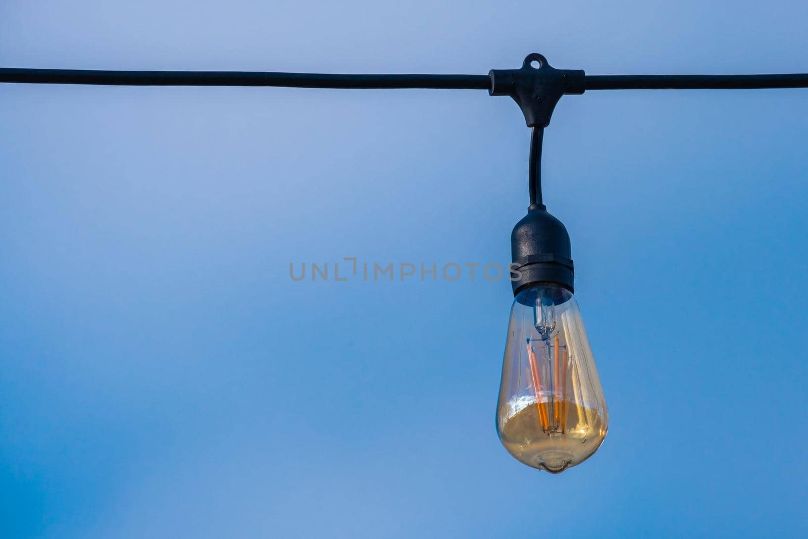 Hanging outdoor light bulb suspended in blue sky by colintemple
