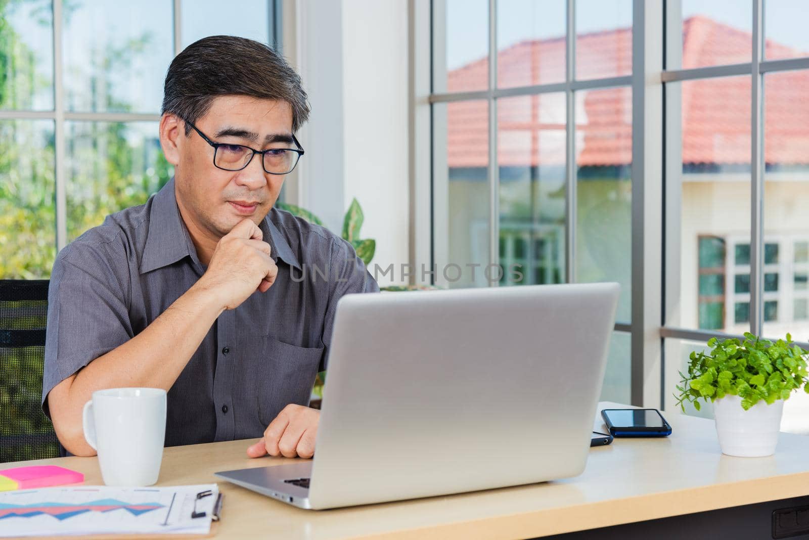 Asian senior business man working online on a modern laptop computer he looking at the screen for remote online studying. Old businessman people using the laptop to video call conference on desk table