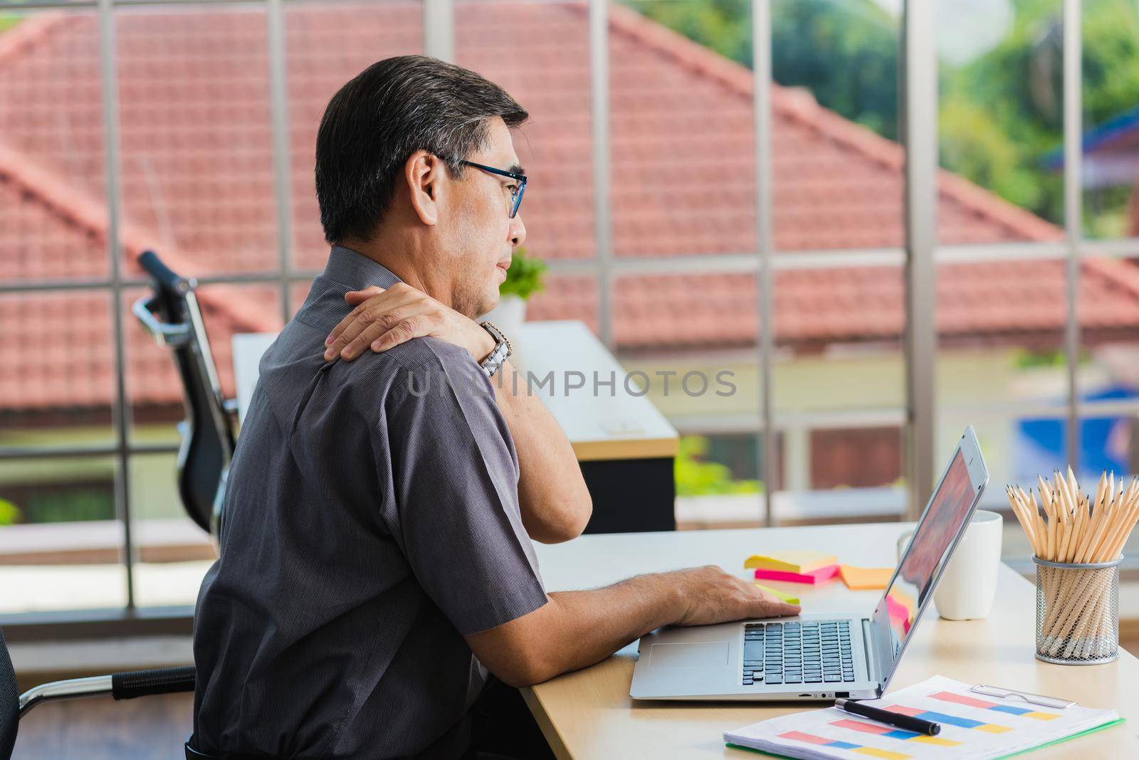 Asian hard senior businessman working with laptop computer has a problem with shoulder pain. Old man feeling pain after sitting at desk long time, Healthcare and medicine office syndrome concept