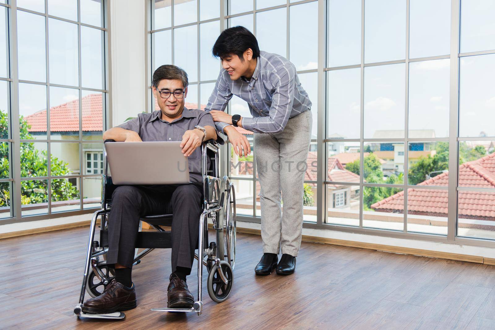 father man sitting wheelchair and his son talking video calls conference on laptop by Sorapop