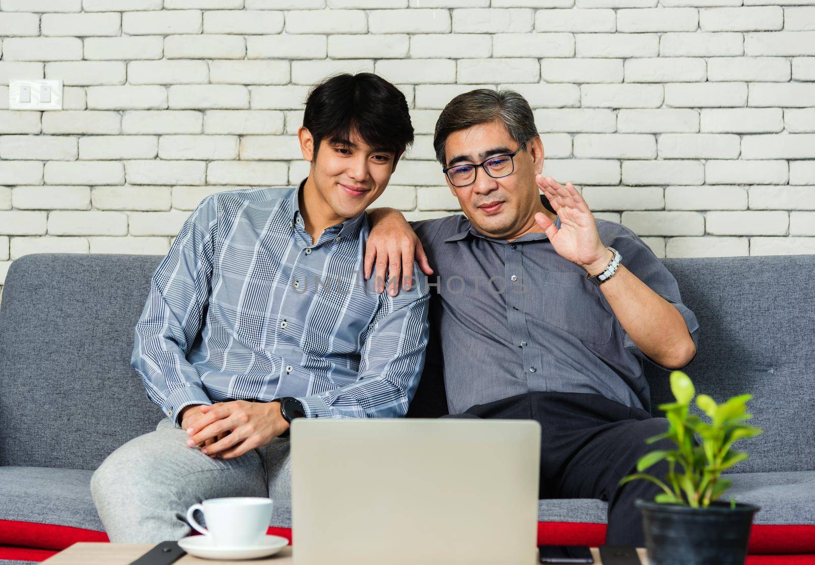 Father man and his son sit on sofa talking chatting on video call by Sorapop